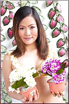  holding plant pots in front of her chest purple and white flowers hair falling down over her shoulders
