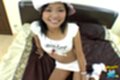 Tun sitting on bed wearing white top in short skirt