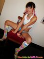 Seated on chair hair in pigtails wearing pink hoop earrings in white cropped top in green shorts wearing floral socks